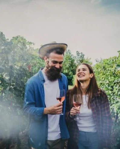 Dos personas ríen con una copa de vino rosado en la mano, entre las hileras de un viñedo