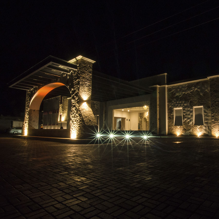Entrada de una vinícola iluminada de noche, con un arco de piedra que deja ver una luz anaranjada y un patio empedrado al frente.