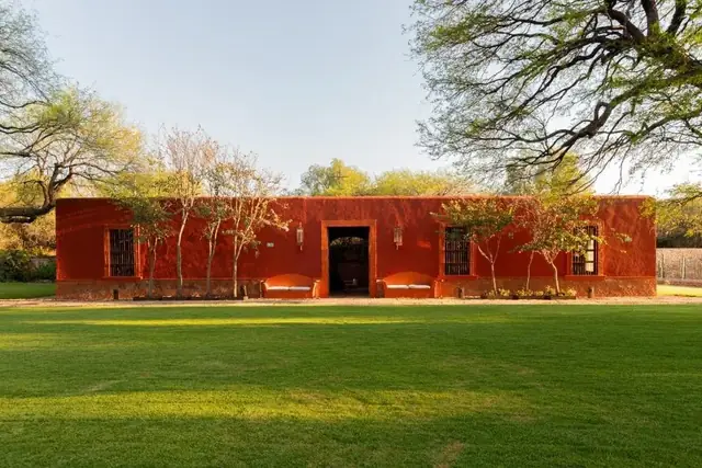 Fachada roja y jardín de la finca, en Casa de Quino