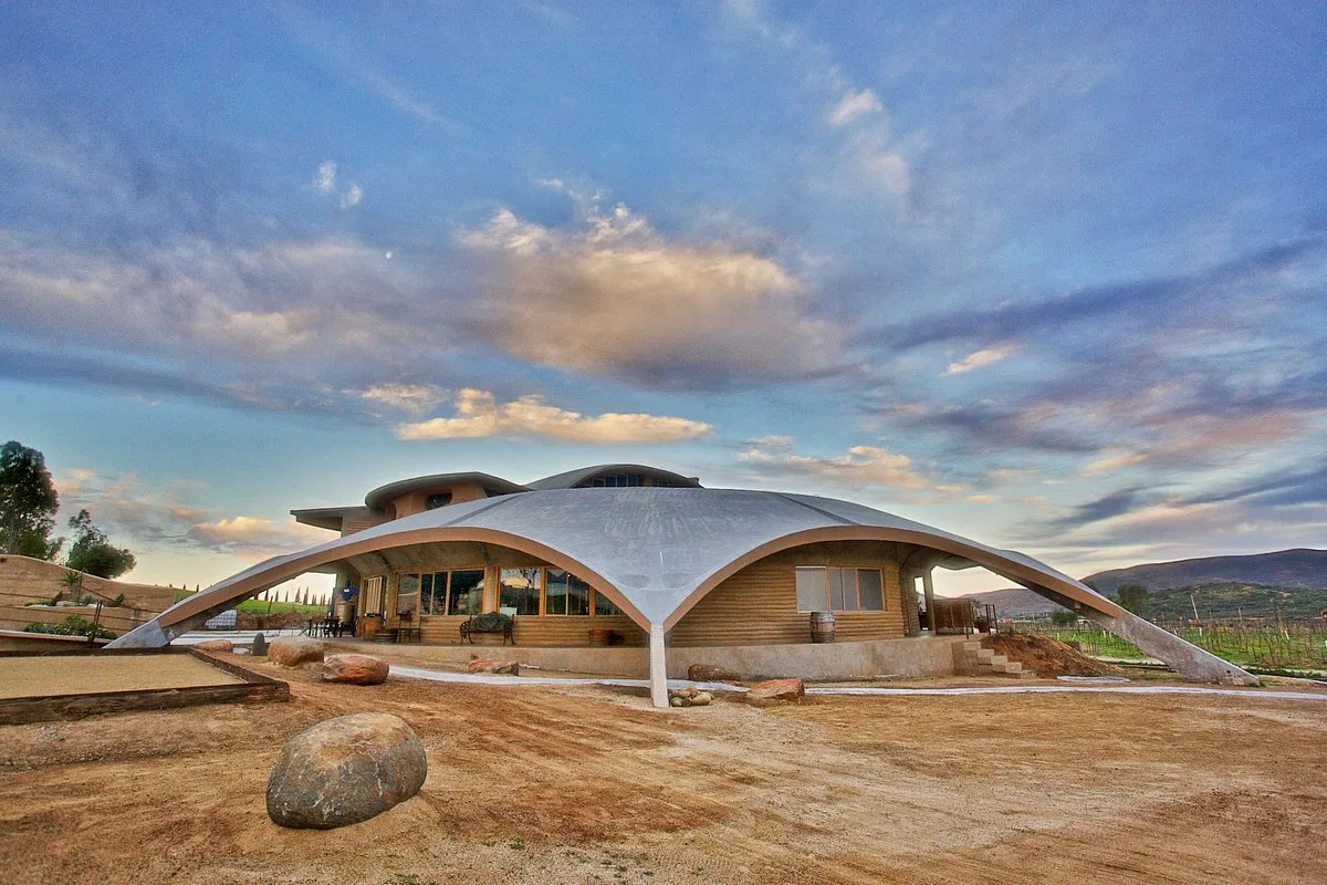 Bodega de Alximia en el Valle de Guadalupe, con techo curvo de concreto que baja hasta el suelo, bajo un cielo con nubes al atardecer